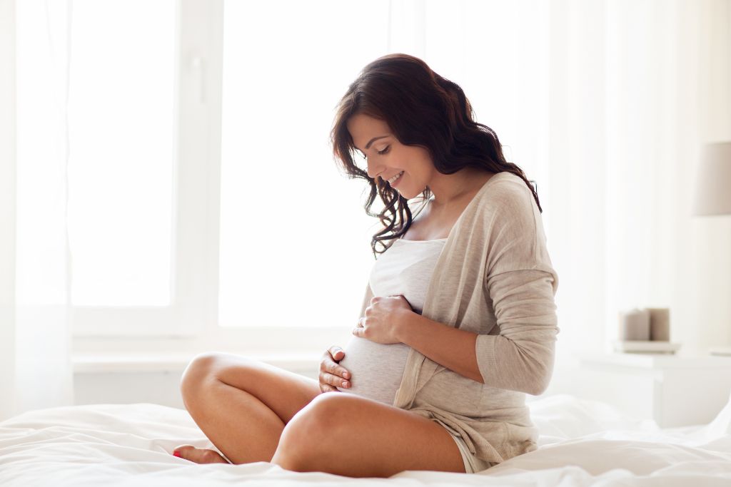 happy pregnant woman sitting on bed at home