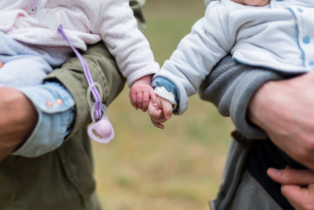 Two babies holding hands while being held by their parents