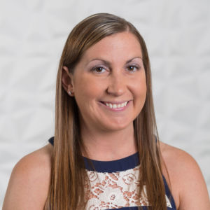 Julie Skripka smiling headshot wearing a navy, white and gold pattern shirt in front of a white background