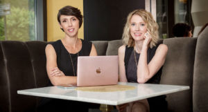 Kristin Revere and Alyssa Veneklase of Gold Coast Doulas sit in a booth seat in front of an open laptop