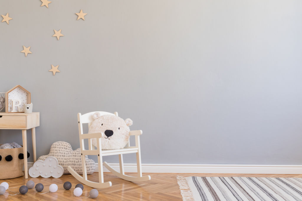 Stylish scandinavian newborn baby room with toys, children's chair, natural basket with teddy bear and small shelf. Modern interior with grey background walls, wooden parquet and stars pattern.