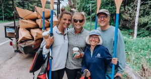 Savannah Tallman family photo in front of stacked kayaks and holding paddles