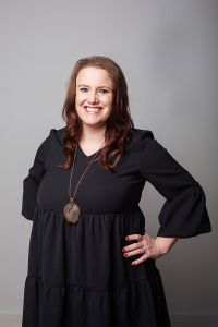 Audra Geyer wearing a black dress and long necklace with her hand on her hip for Gold Coast Doulas