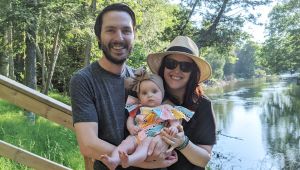 Audra of Gold Coast Doulas with husband and infant daughter standing in front of a river and wooded area together