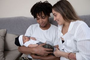 Smiling couple holds their newborn baby on a couch together