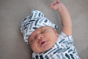 Swaddled newborn in matching hat with his arm out of the swaddle