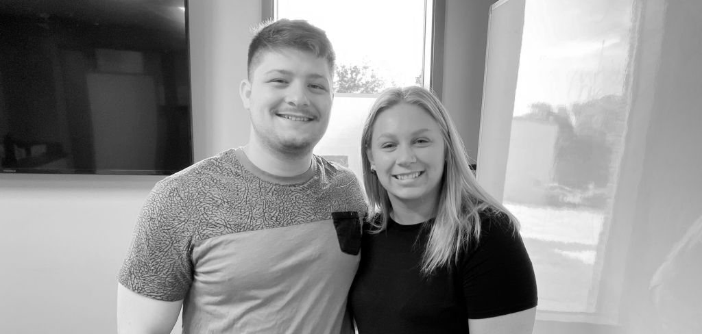 Olivia Gibson poses with a man in front of a TV and window in black and white