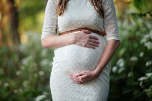 Body shot image of a pregnant woman holding her baby bump in front of greenery