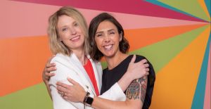 Kristin and Alyssa of Gold Coast Doulas giving a side hug in front of a colorful wall