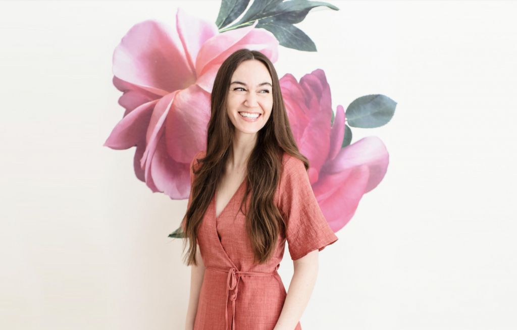 Woman wearing a mauve jumper poses in front of a floral mural