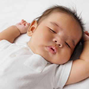 Sleeping baby wearing a white onesie on a white bed