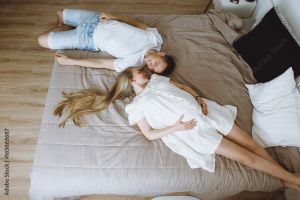 Couple laying on a bed looking at one another while the woman cradles her pregnant belly