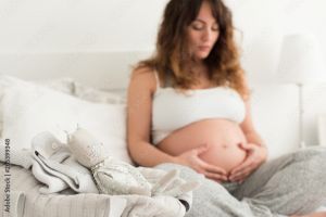 Pregnant woman sitting on a bed cradling her pregnant belly while breathing
