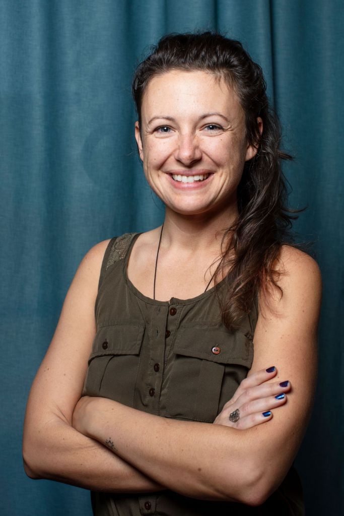 Ashley H of Gold Coast Doulas poses with her arms crossed in front of a blue curtain