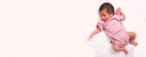 Newborn wearing a pink onesie laying on a white bed sheet