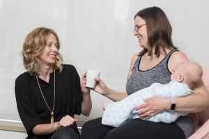 Kristin Revere handing a mug to a mother holding her infant