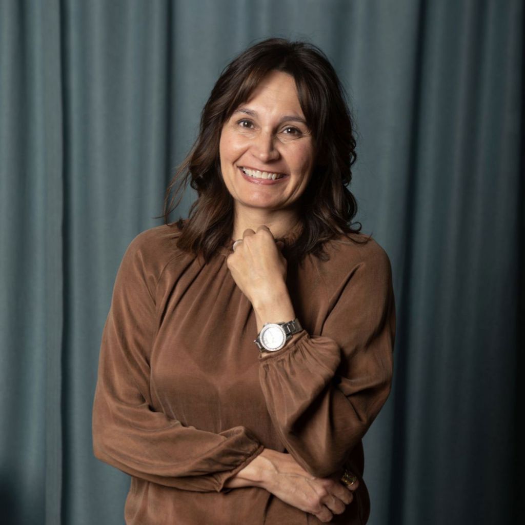 Lisa Newhouse poses in front of a blue curtain wearing a brown top