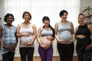 Five pregnant women standing together cradling their pregnant bellies