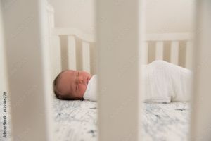 Sleeping newborn baby in a white swaddle rests in a white crib
