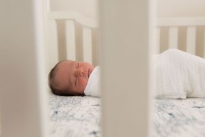 Sleeping newborn baby in a white swaddle rests in a white crib