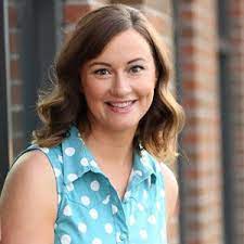 Carrie from MomsBloom poses in front of a brick wall wearing a teal button up tank top with white polka dots