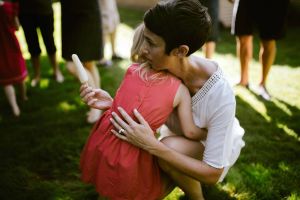 Woman holding a popsicle kneeling down to hug a child in the grass surrounded by people