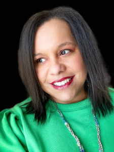 Erica wearing a green sweater with a blue and white beaded necklace against a black wall