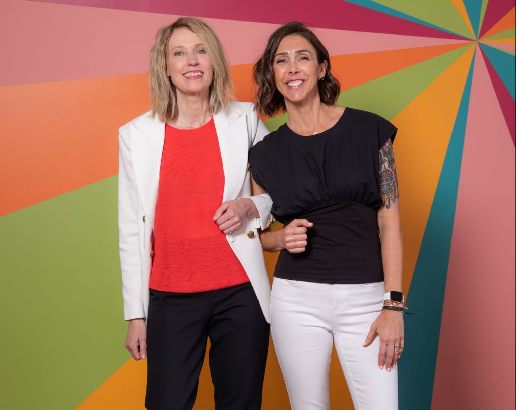 2 women in professional clothes with a colorful geometric background