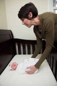 Alyssa from Gold Coast Doulas places a sleeping and swaddled infant into a crib