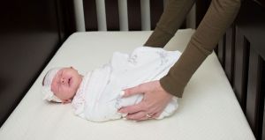 Woman's hands gently placing a swaddled and sleeping infant in a crib