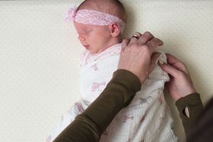 Woman swaddling a sleeping infant on a crib mattress