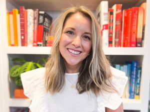 Linzay wearing a white top smiles in front of a colorful bookcase