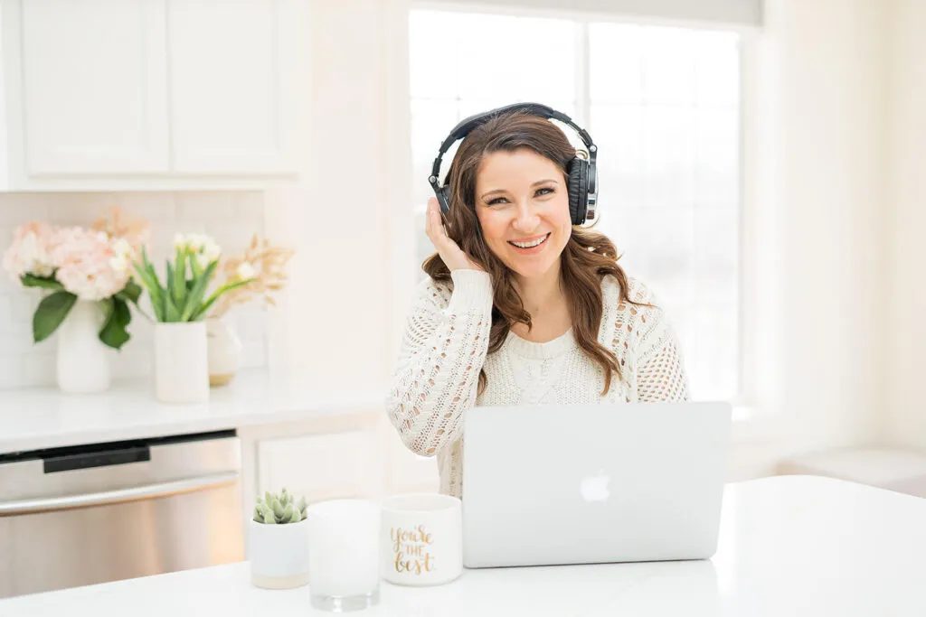 Elizabeth sits at a kitchen counter with headphones and a laptop