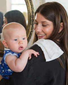 Mother wearing a black shirt holds a baby with a burp cloth on her shoulder and a mirror in the background