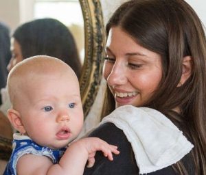 Mother wearing a black shirt holds a baby with a burp cloth on her shoulder and a mirror in the background
