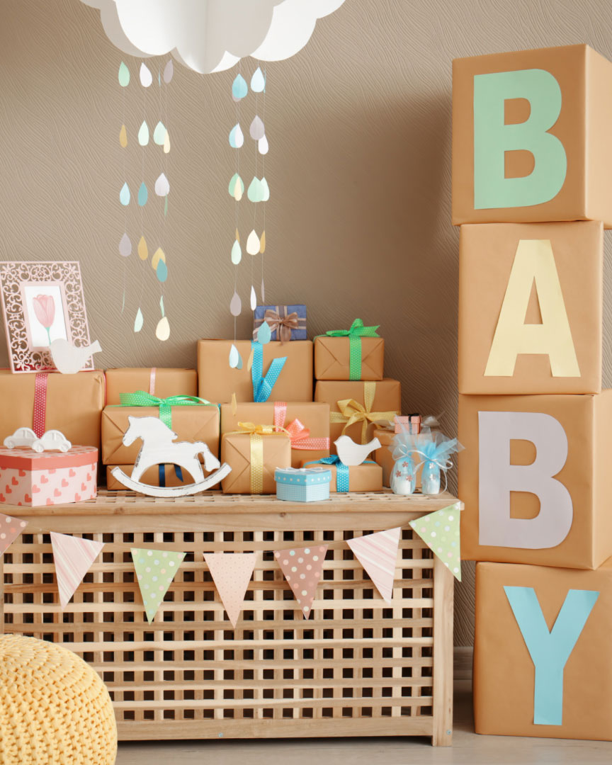 Boxes stacked spelling out baby to the right of the image with a table full of presents for a baby shower