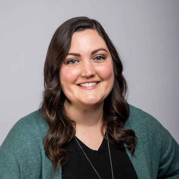 Kristin Morter from Gold Coast Doulas smiles wearing a black v-neck shirt and teal cardigan with a grey background headshot