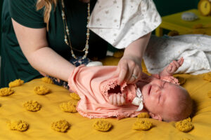 Woman dressing a fussing baby on a yellow bed