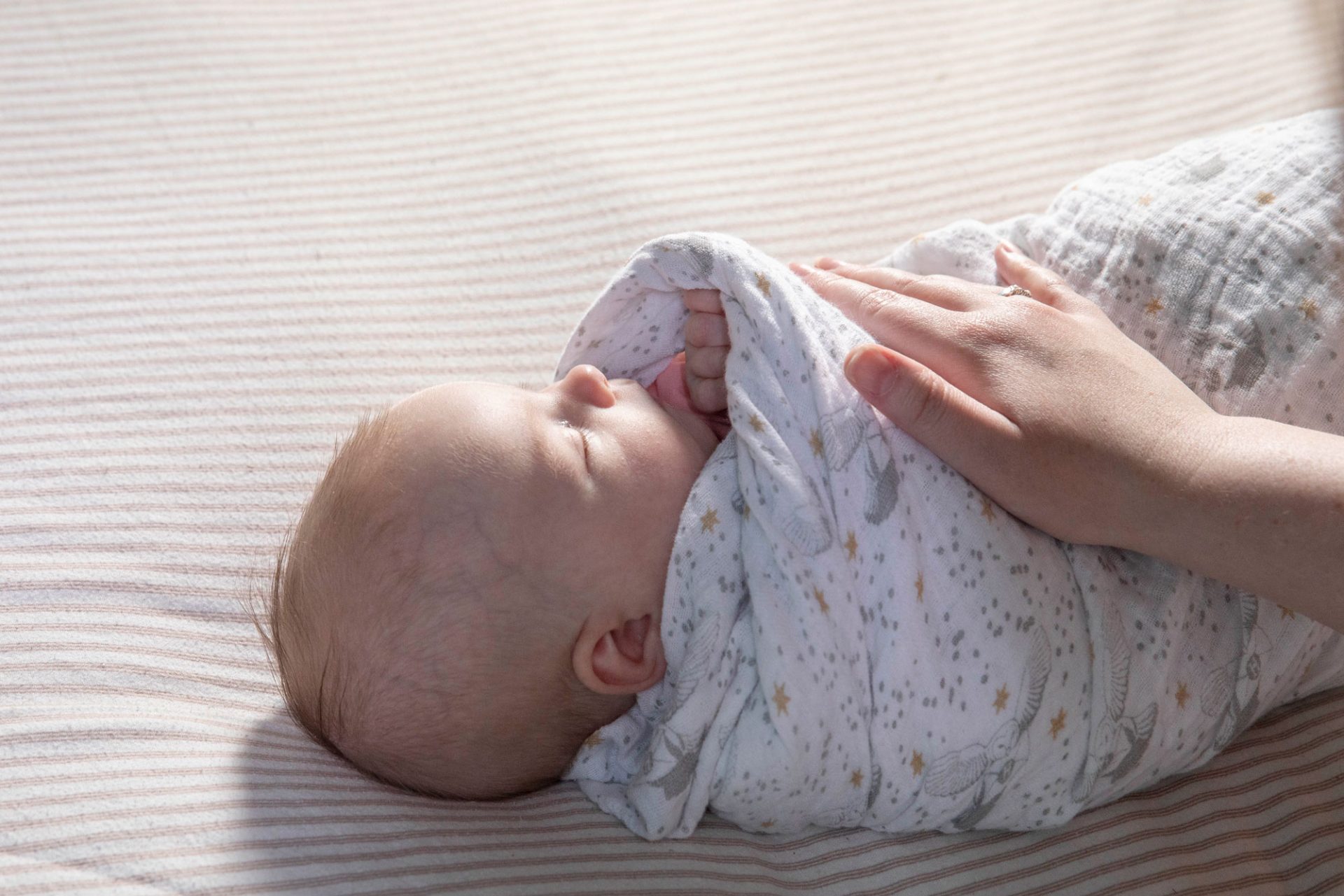 Swaddled and sleeping baby with a hand resting on them