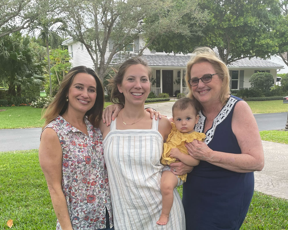 Jackie Viscusi from Gold Coast Doulas holding a baby outside with two women on either side of her and a home in the background