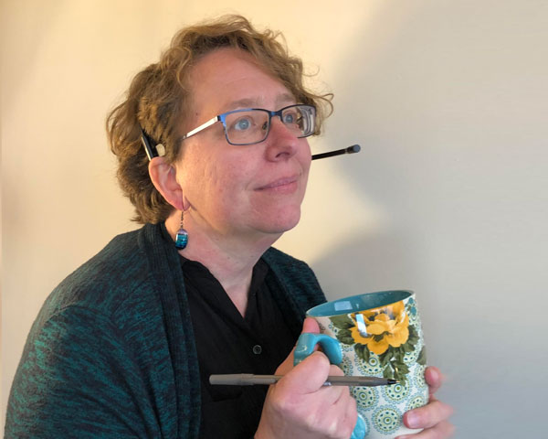 Deb Porter wearing a headset, holding a coffee mug with pen against a white wall