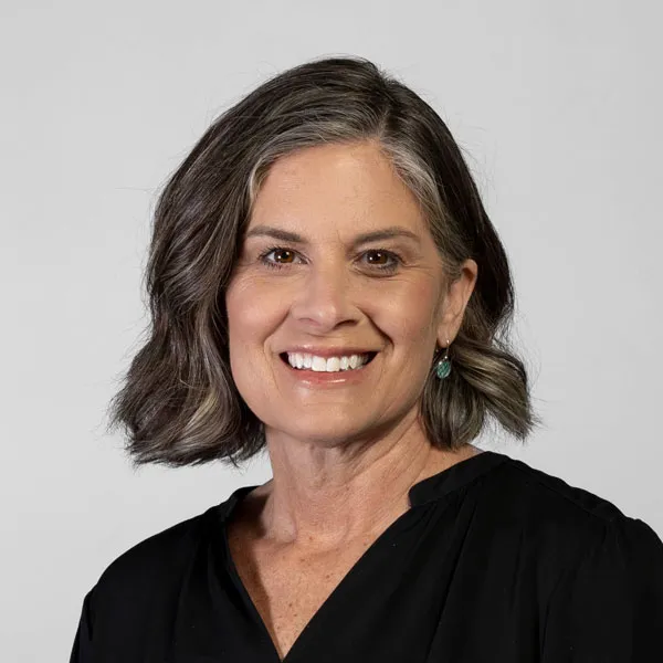 Krista Batdorff, Bed Rest & Postpartum Doulas, of Gold Coast Doulas poses against a grey backdrop wearing a black blouse headshot