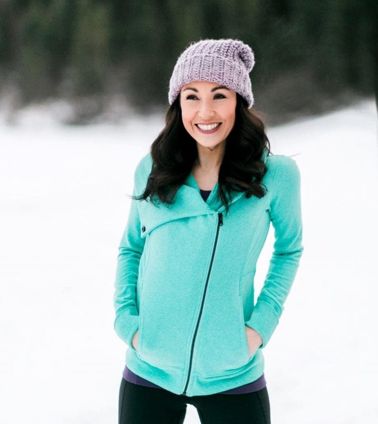 Amanda Koch wearing a teal jacket with a purple knit hat standing in snow