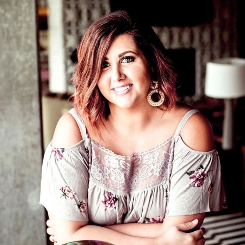 Jenni Froment of VBAC Academy wearing a floral top with striped rug and white lamp in the background