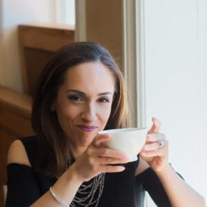 Melissa Llarena, author and coach, holds a white coffee mug wearing a black top and beaded necklace