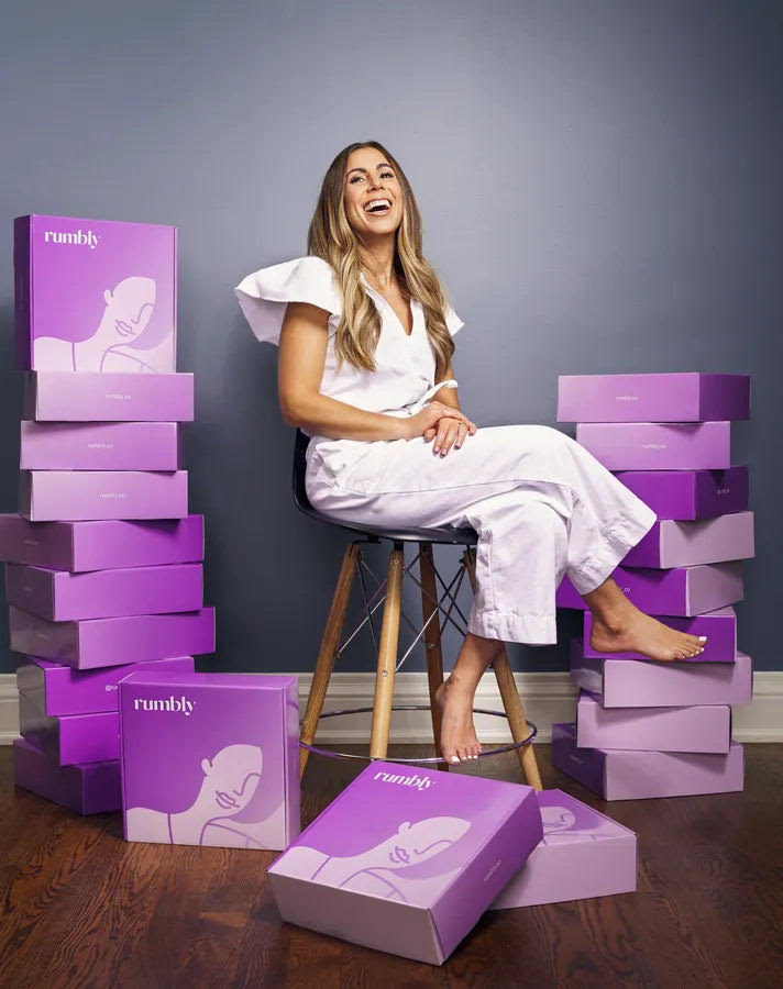 Marnie of Rumbly, a pregnancy subscription box company, sits surrounded by purple Rumbly boxes.