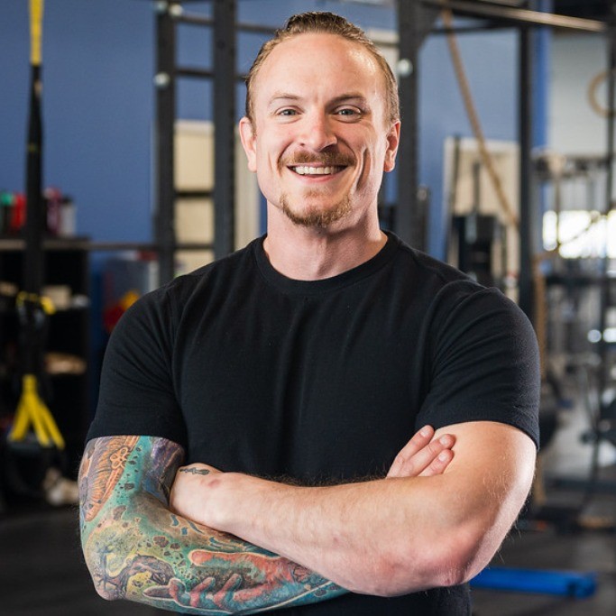 Josh Dech poses cross armed and in a black t-shirt in front of exercise equipment