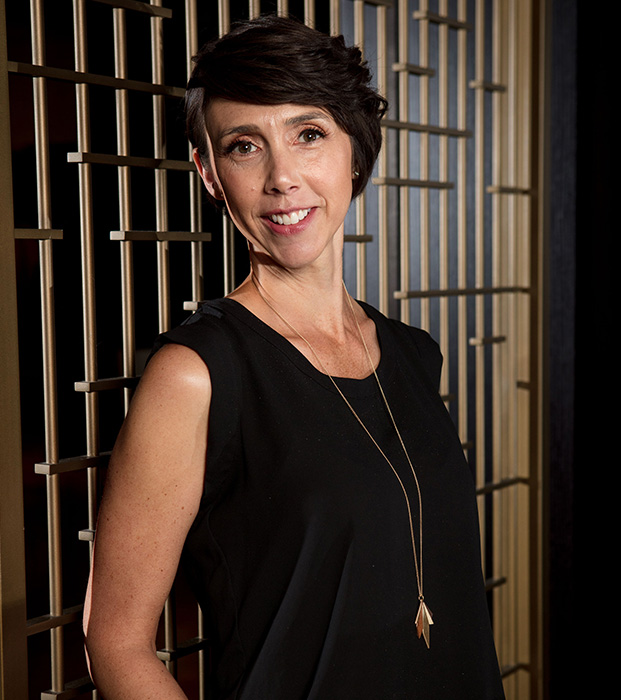 Alyssa Veneklase in black dress standing in front of gold and black. background