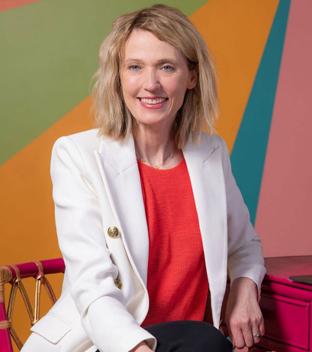 Kristin sitting in white jacket in front of colorful geometric background