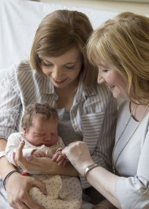 Mom and grandma smiling while they hold a baby